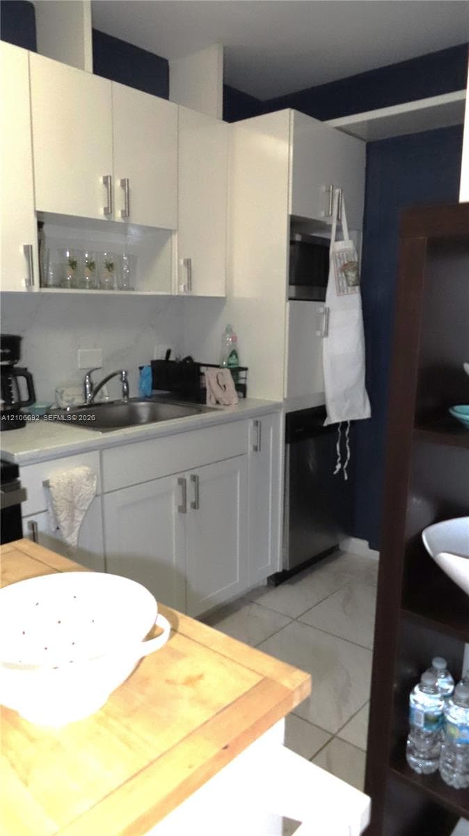 Kitchen featuring white shaker-style cabinetry, stainless steel appliances, a stainless steel sink with a pull-down faucet, and light-toned tile flooring