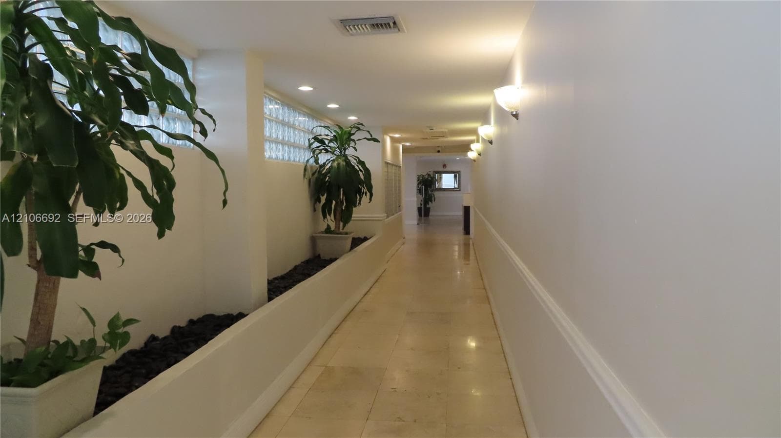 Hallway featuring tiled flooring, recessed ceiling lighting, wall-mounted sconces, and interior glass block detailing