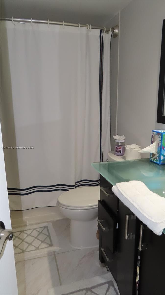 Bathroom featuring dark cabinetry with brushed metal hardware, a frosted glass countertop, and tiled flooring