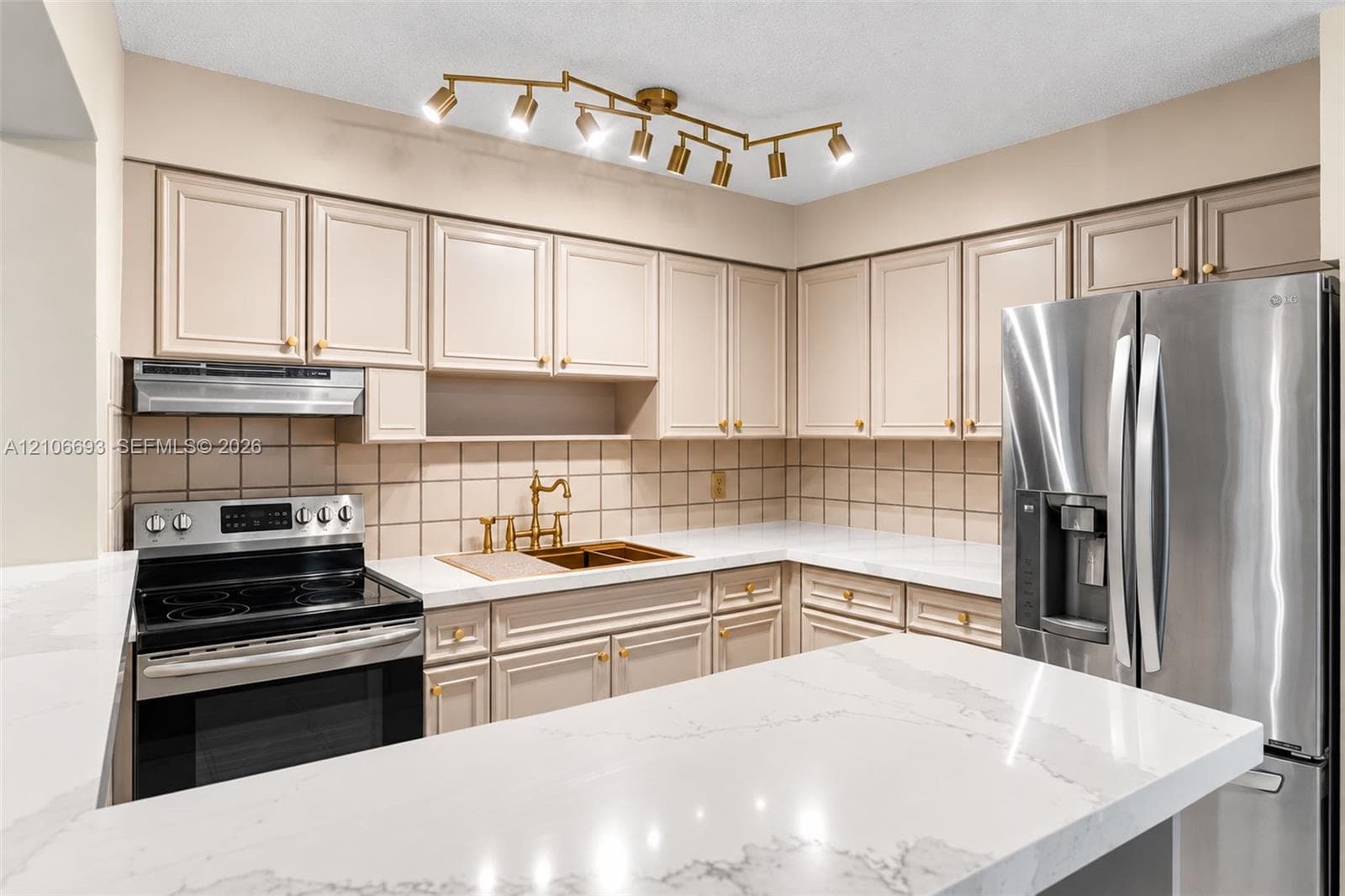 Kitchen featuring quartz countertops, shaker-style cabinetry, a multi-light directional ceiling fixture, stainless steel appliances, and a tiled backsplash