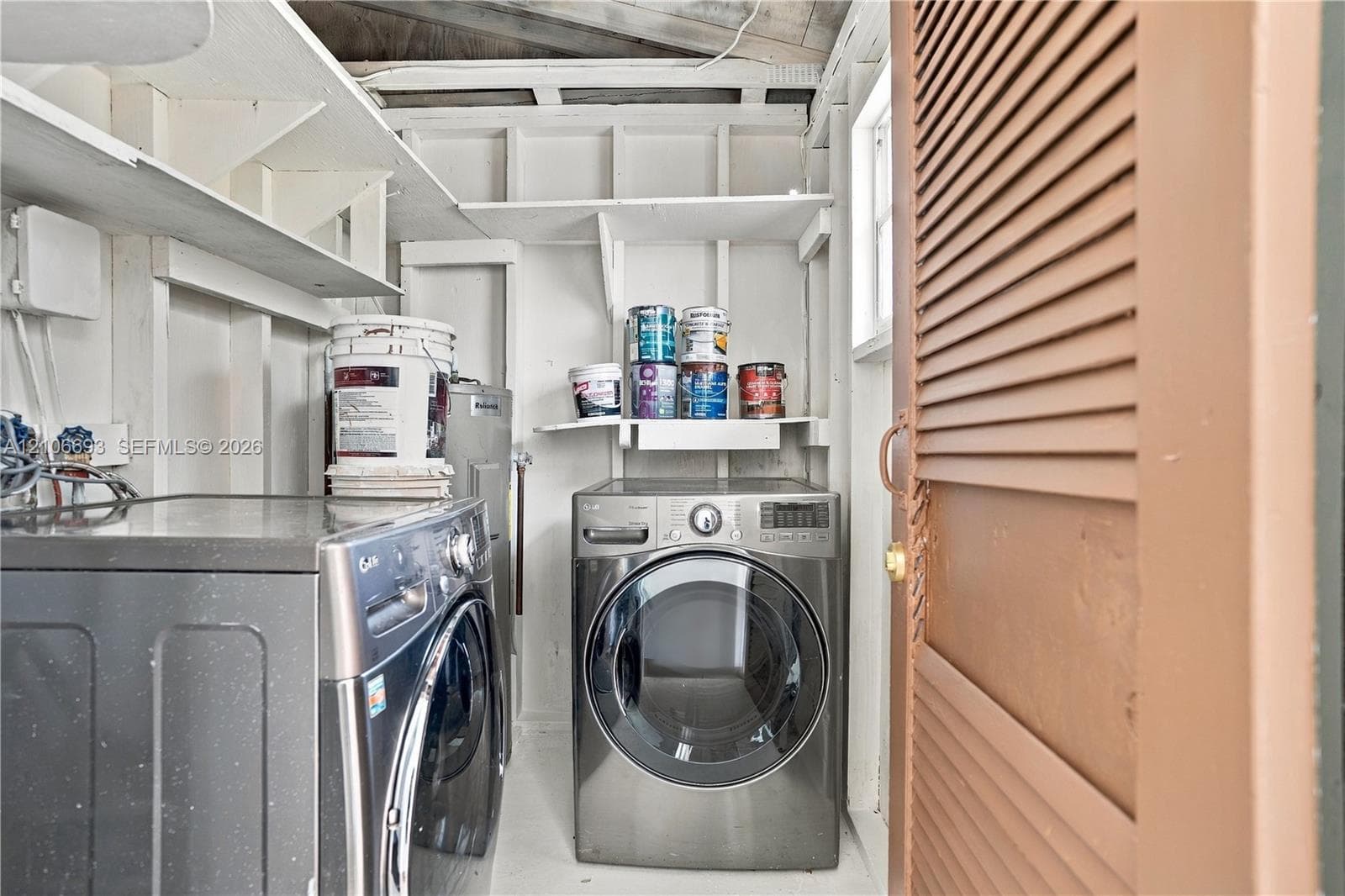 Laundry space featuring built-in open shelving, louvered door, and exposed structural framing