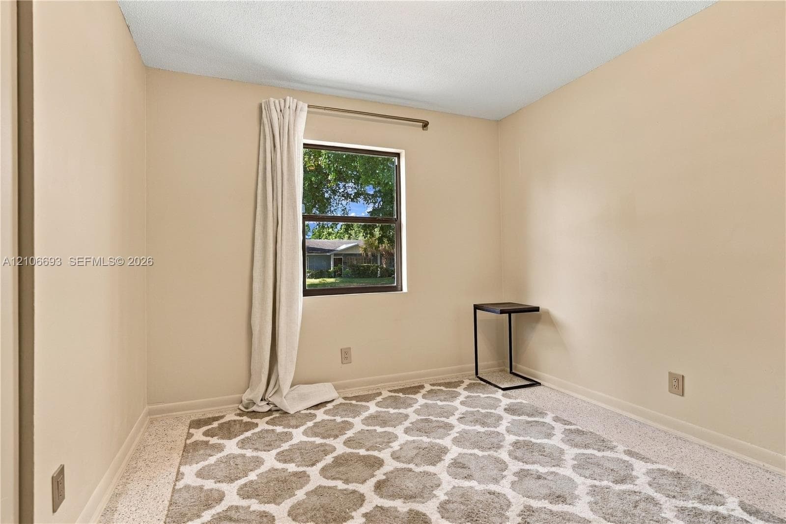 Neutral-toned room featuring a single-pane window with dark trim, textured ceiling, and terrazzo flooring