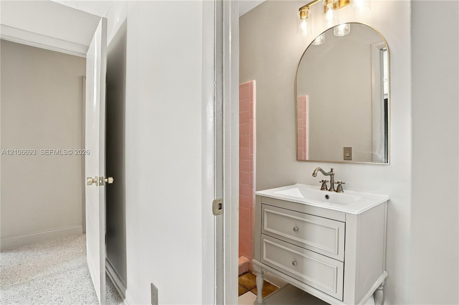 Bathroom featuring a vanity with two drawers and an integrated countertop, arched wall mirror, three-light vanity fixture, and pink tiled wall accents