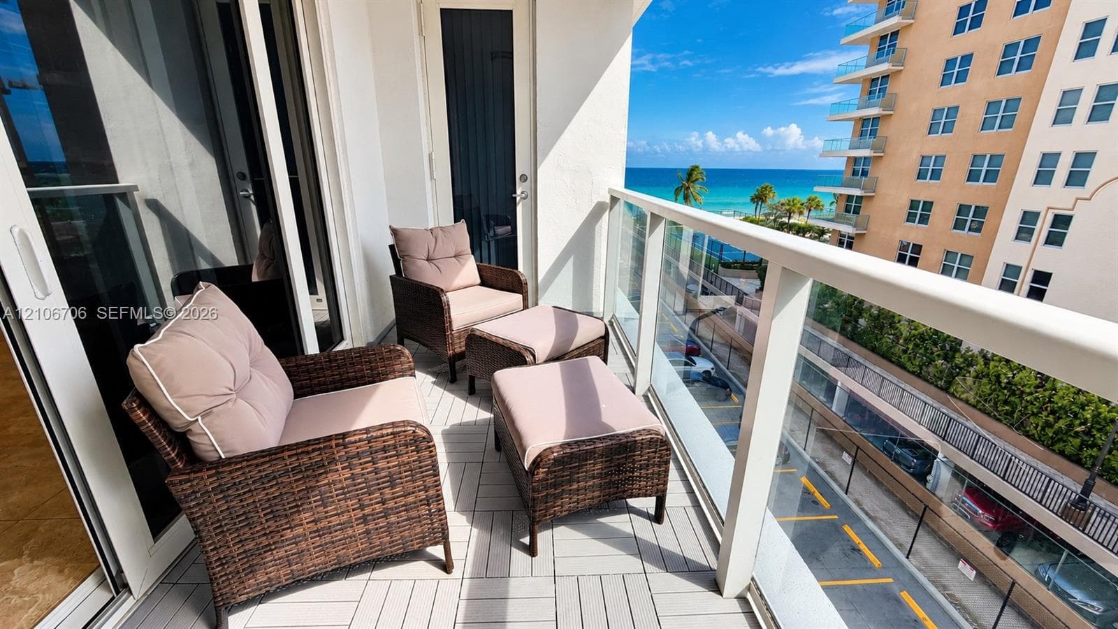 Private balcony featuring light-toned modular deck tiles, white metal railings with glass panel inserts, and direct access through large sliding glass doors
