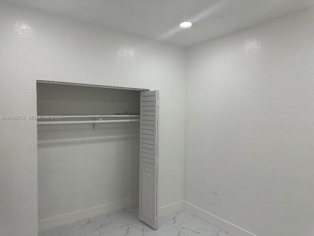 Room featuring white wall-finish, recessed lighting, tile flooring with marble-style veining, and a closet with louvered bifold doors