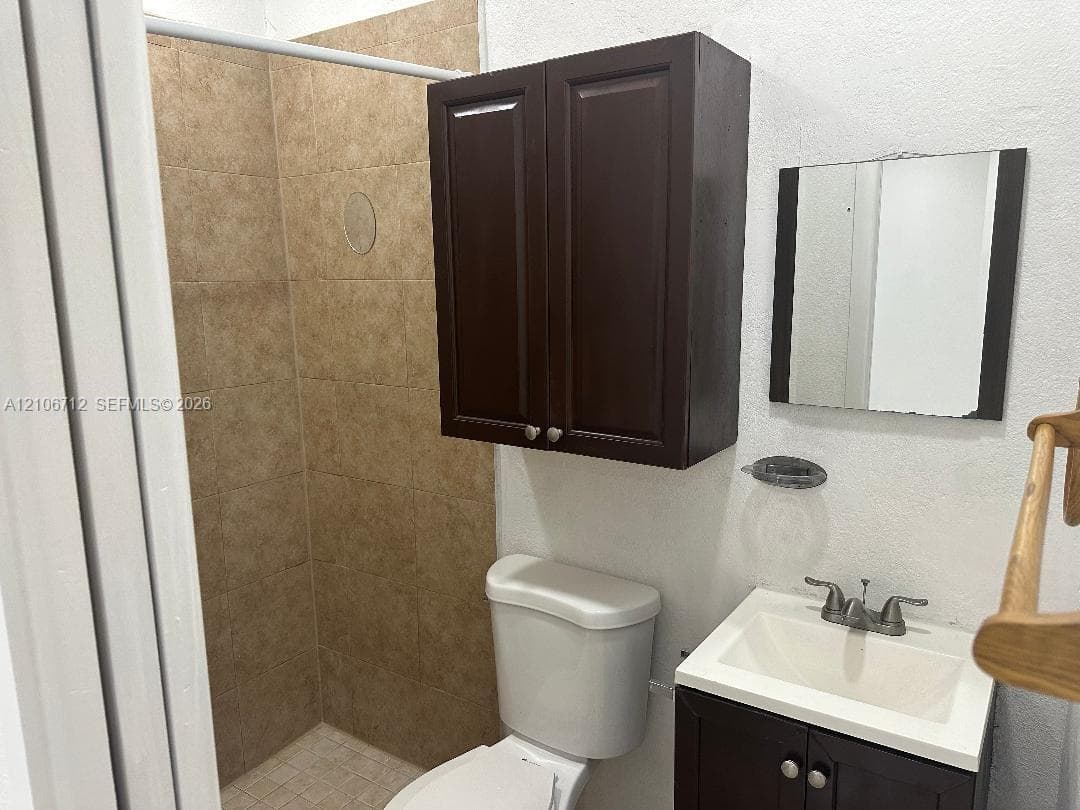 Bathroom featuring a tiled shower enclosure, dark wood-finish vanity with an integrated basin, matching wall-mounted storage cabinet, and a square mirror