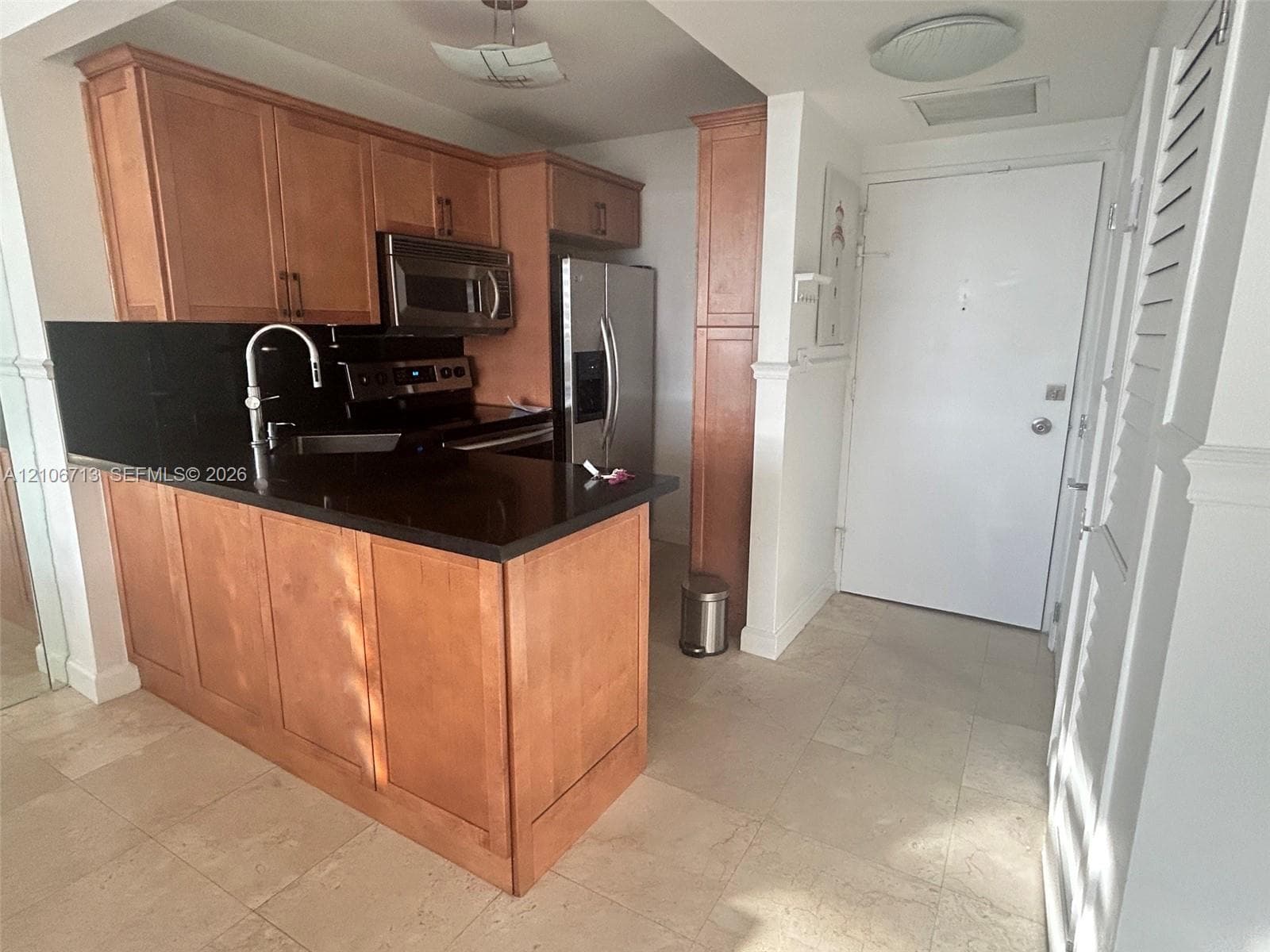 Kitchen featuring shaker-style wood cabinetry, dark stone countertops, stainless steel appliances, and large-format tile flooring