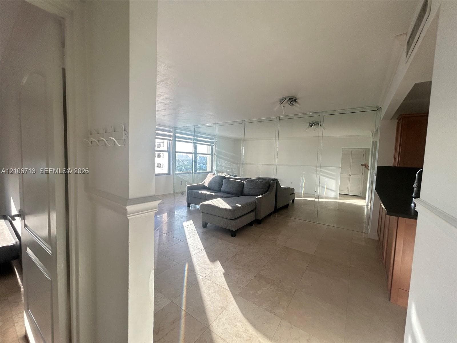 Large-format stone tile flooring, wall-to-wall mirrored panels, natural light through floor-to-ceiling windows, and wood-finish cabinetry with dark countertops
