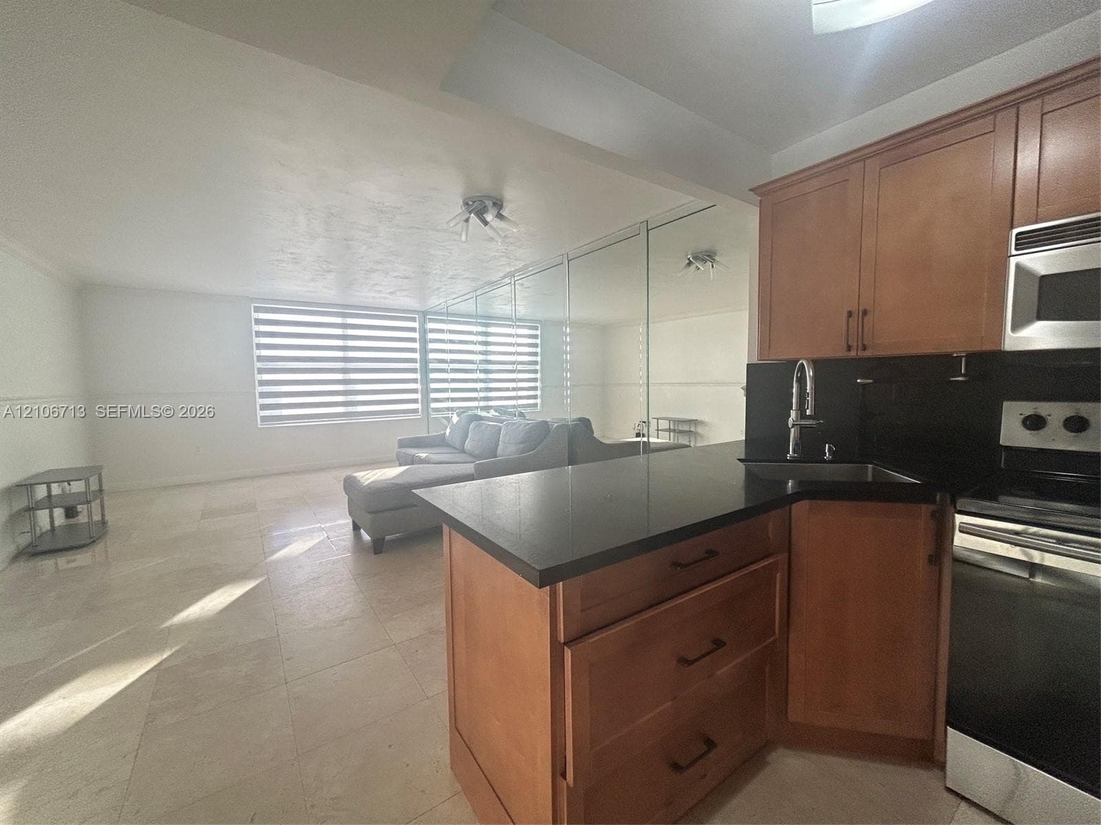 Kitchen featuring wood-finish cabinetry, solid surface countertops, stainless steel appliances, and large-format tile flooring