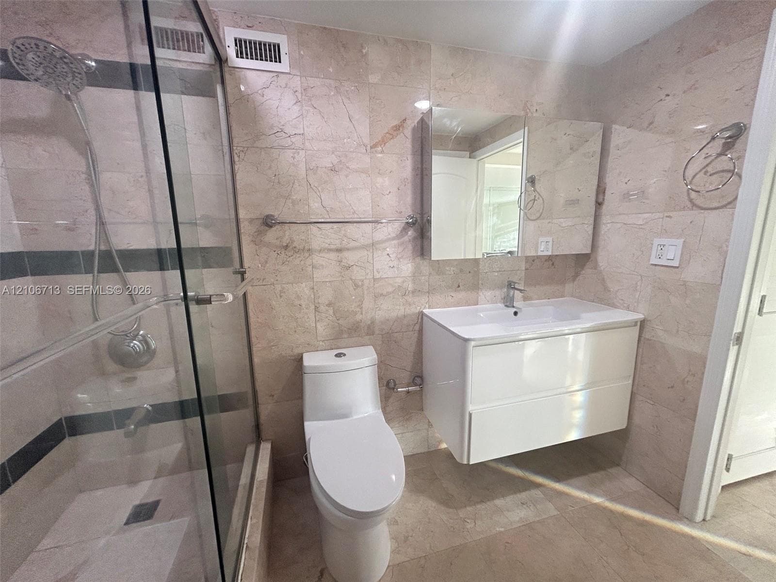 Bathroom featuring floor-to-ceiling stone wall tiling, a floating vanity with a white basin, a glass-enclosed shower with a rainfall showerhead, and a wall-mounted medicine cabinet