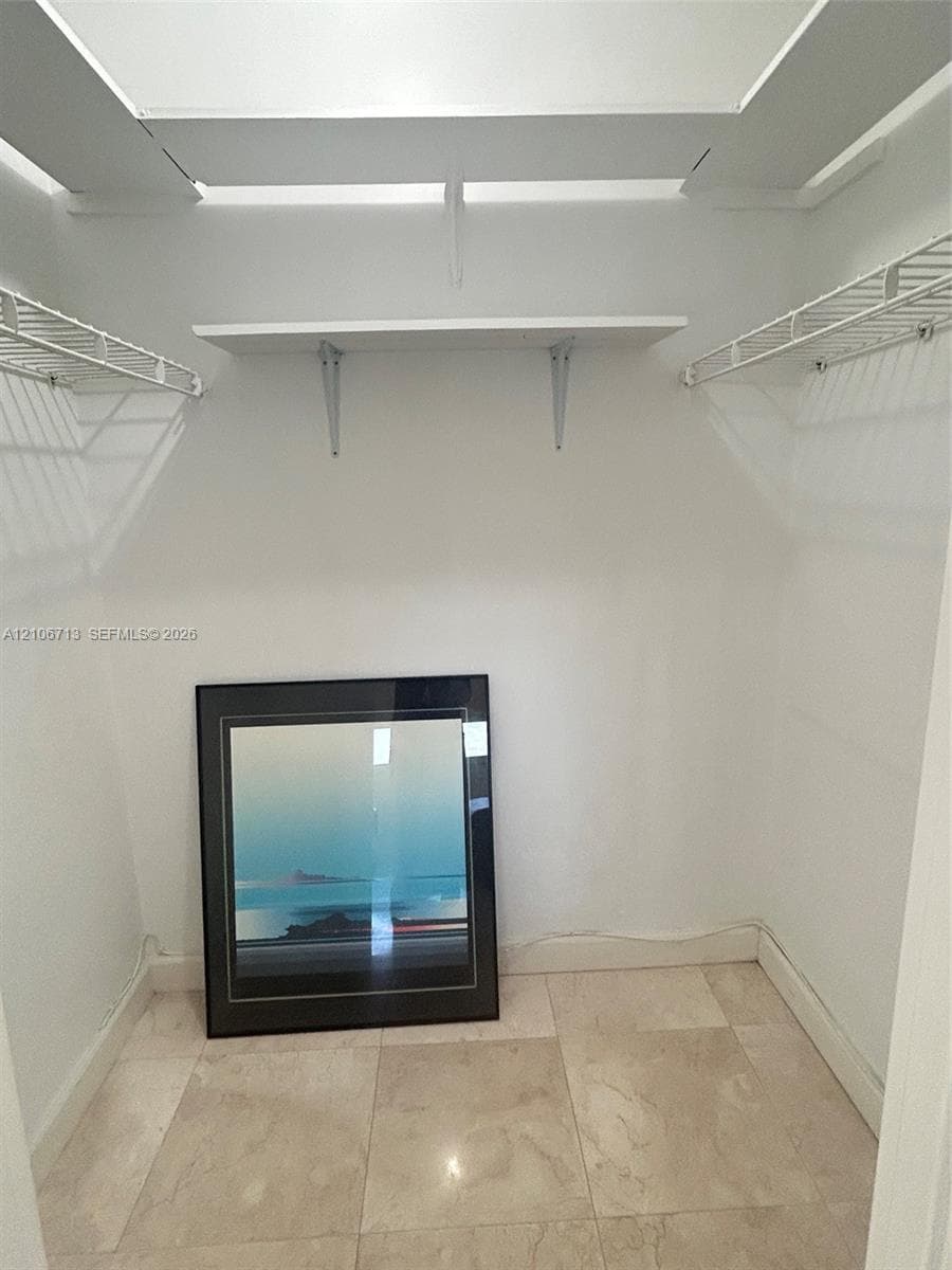Walk-in closet featuring white wire shelving, a centered solid shelving unit, and stone-tile flooring
