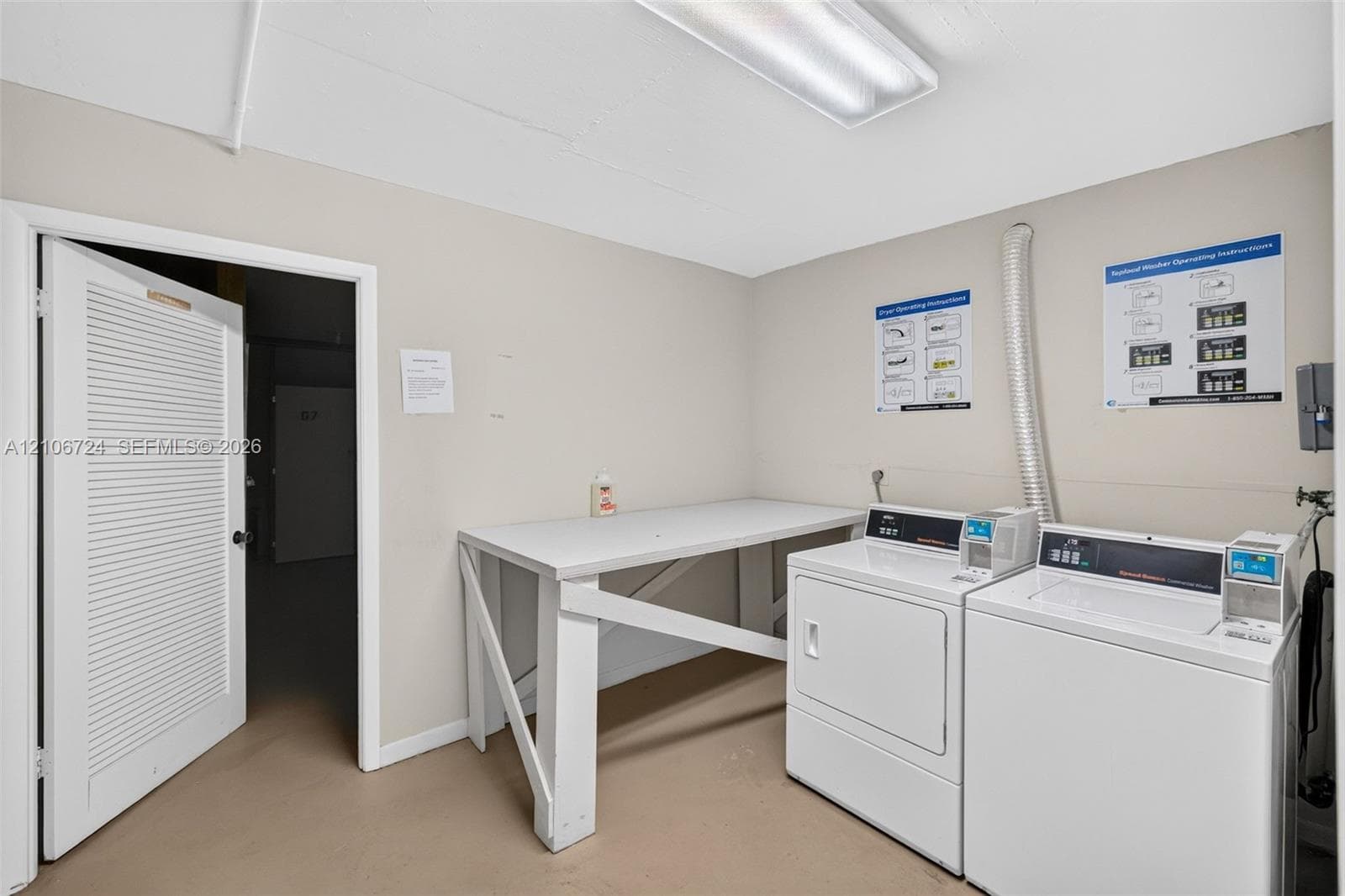 Utility room featuring built-in white folding table, louvered door, and overhead fluorescent lighting