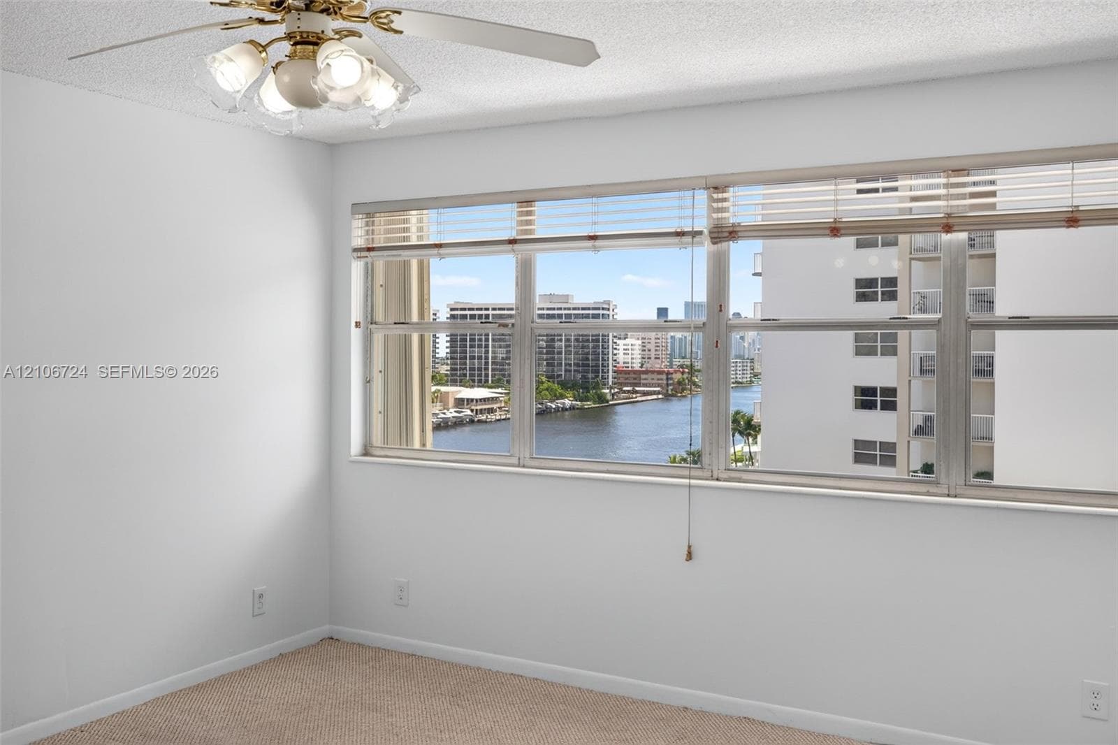 Large windows with horizontal blinds, carpeted flooring, and a ceiling fan with integrated lighting fixtures