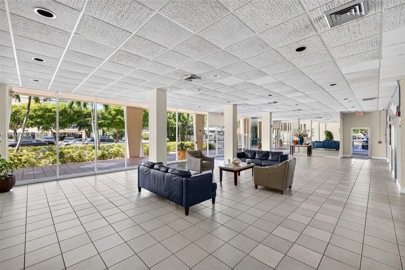 Open-concept interior featuring floor-to-ceiling glass panel walls, square ceramic tile flooring, recessed lighting, and a drop-grid ceiling