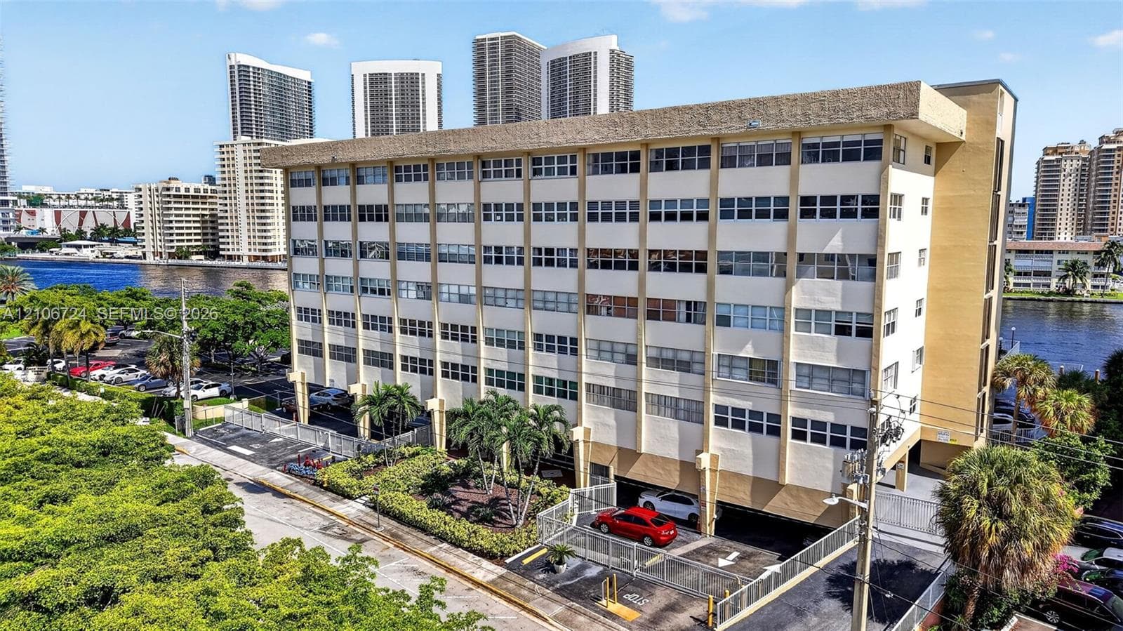 Multi-story residential building featuring a concrete facade, expansive window rows, ground-level covered parking, and perimeter landscaping