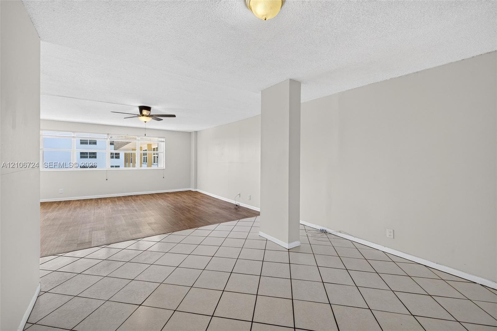 Open-concept interior featuring large-format diagonal tile flooring, wood-finish flooring, a ceiling fan with integrated lighting, and a prominent structural pillar
