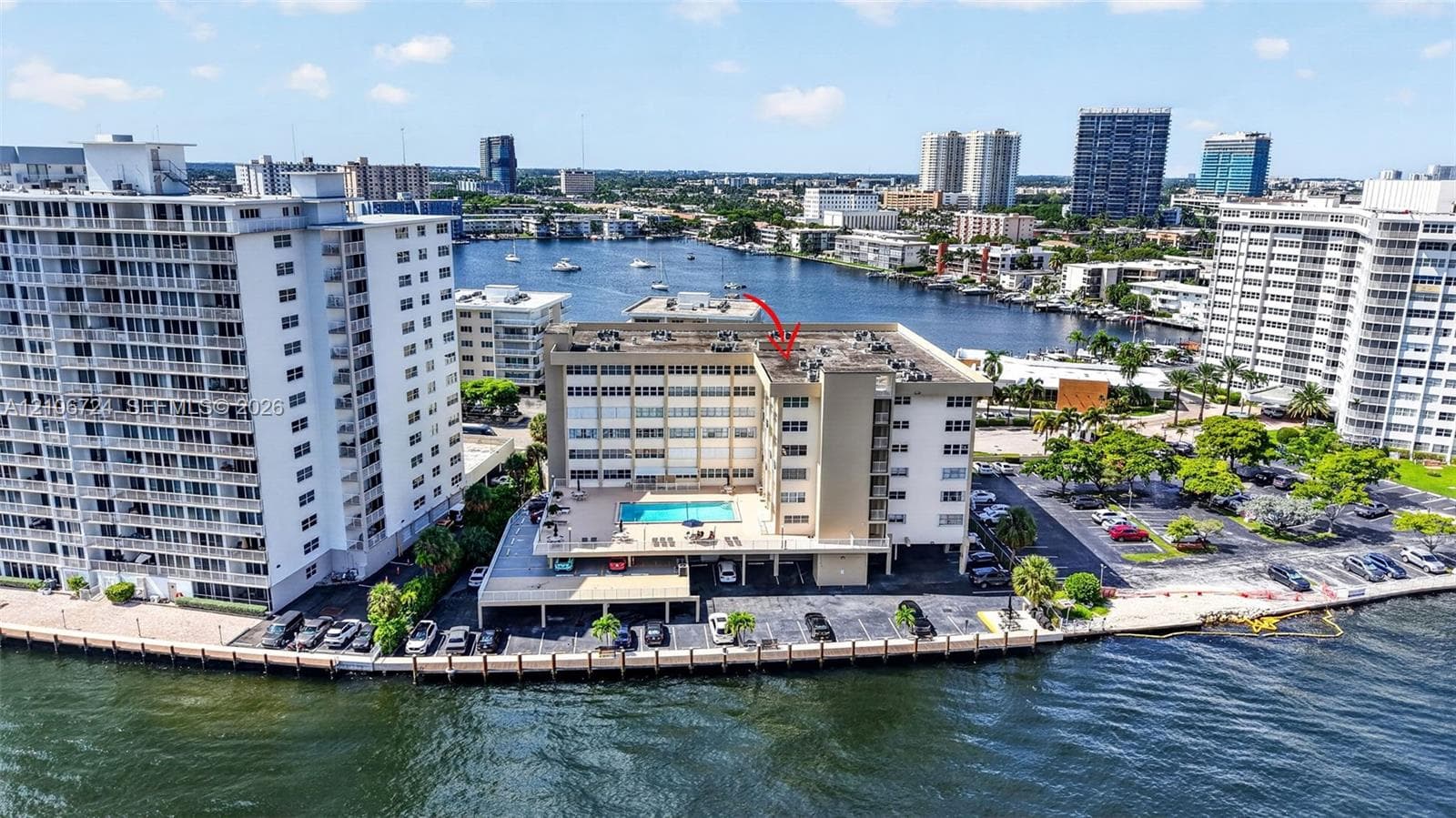 Mid-rise waterfront multi-story building featuring an elevated exterior pool deck, covered parking, and direct water frontage