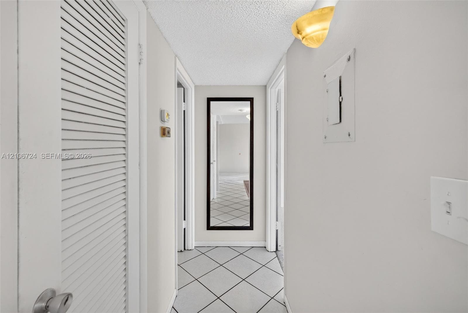 Hallway featuring diamond-patterned tile flooring, louvered closet door, and half-dome wall-mounted light fixture