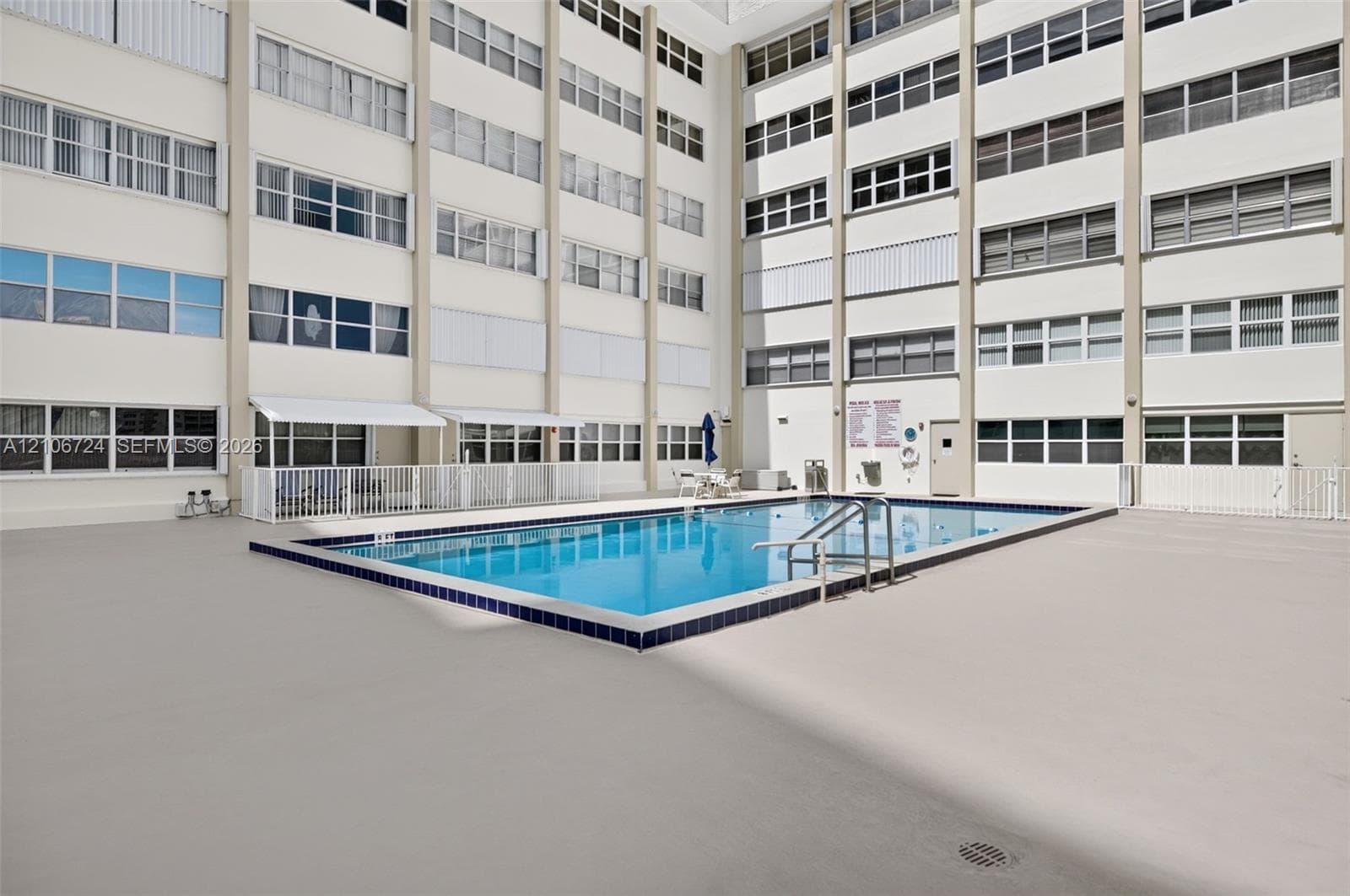 Rectangular swimming pool with tiled coping and integrated metal handrails, set within a spacious concrete deck surrounded by multi-story residential architecture