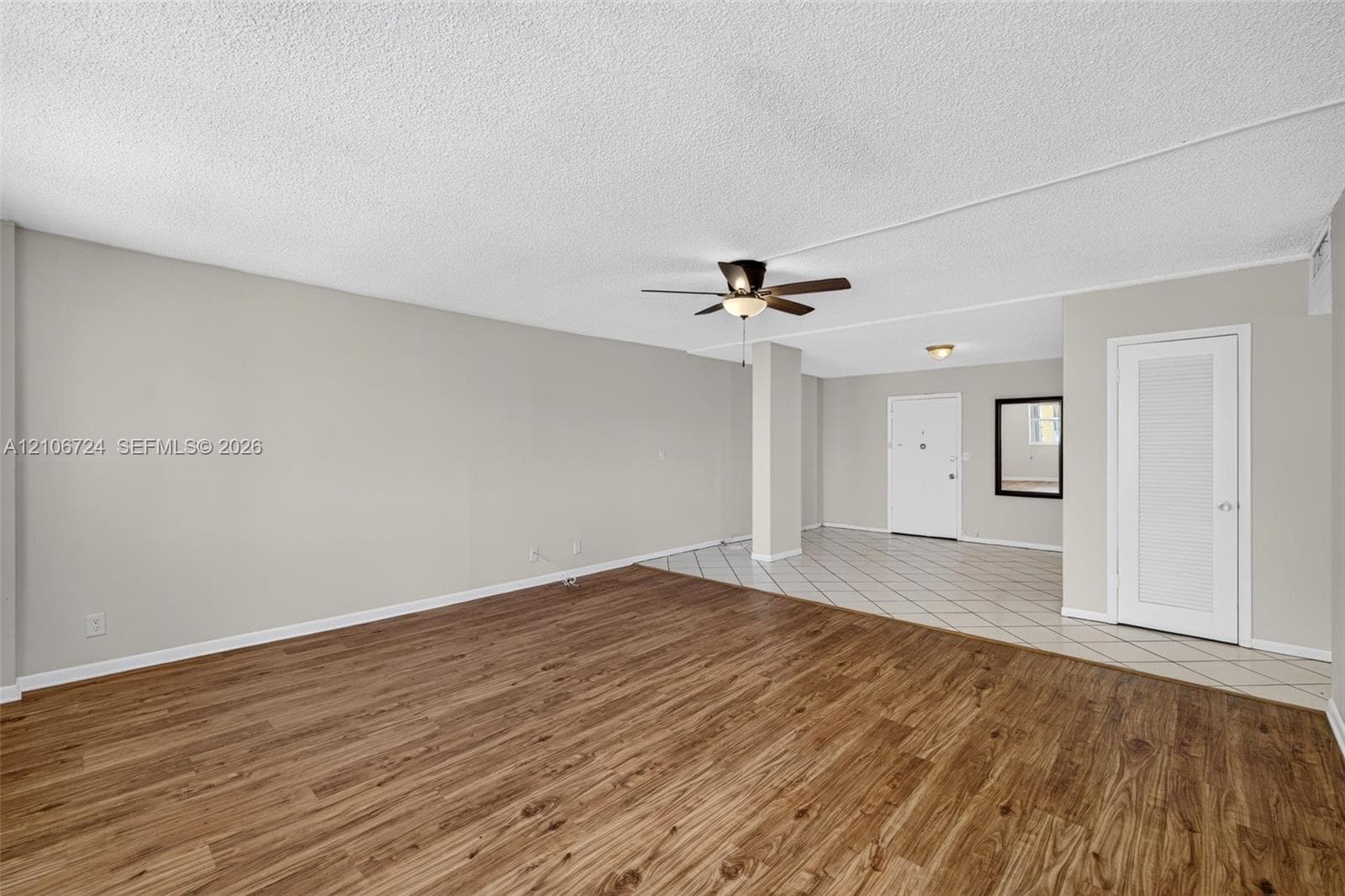 Open interior space featuring wood-finish flooring, neutral wall paint, tiled entryway, ceiling fan with integrated lighting, and a six-panel louvered closet door
