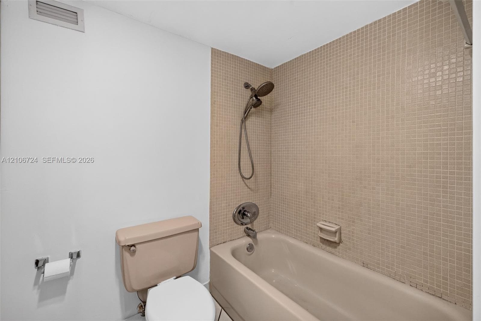 Bathtub with a shower head, tiled surround, and chrome hardware