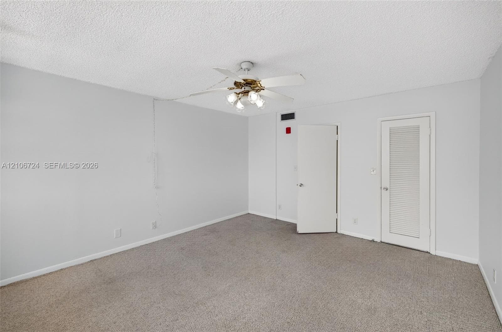 Interior space featuring neutral wall tones, carpeted flooring, a ceiling fan with integrated lighting, and a louvered door