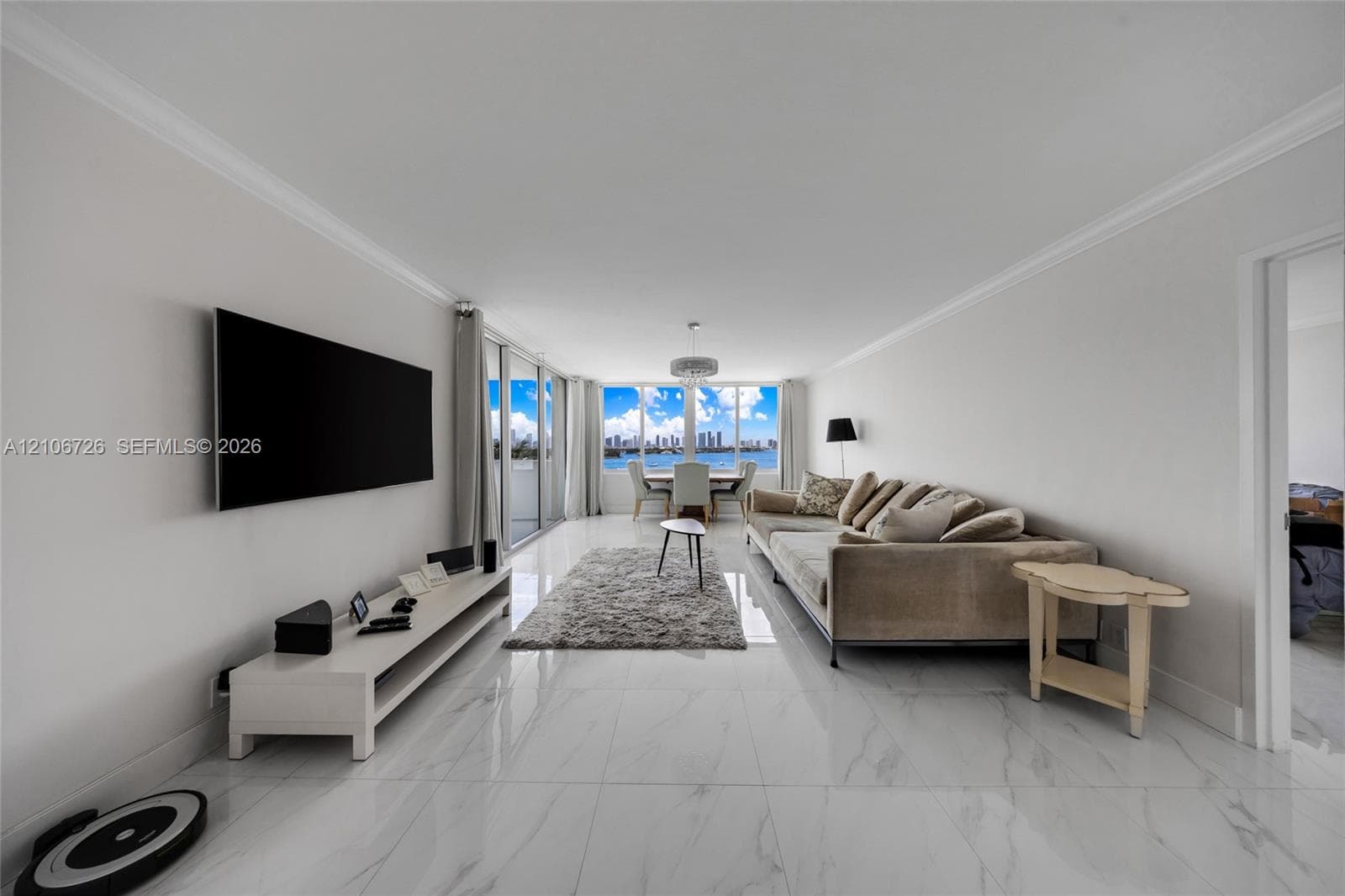 Open-concept living space featuring large-format tile flooring with marble-finish veining, floor-to-ceiling glass sliding doors, and water and city skyline backdrop