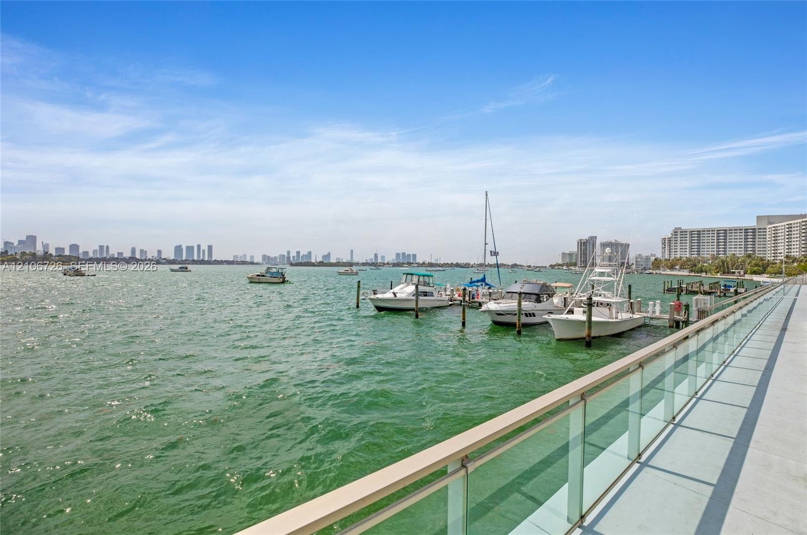 Waterfront promenade featuring a glass-panel railing, concrete walkway, and private boat slips