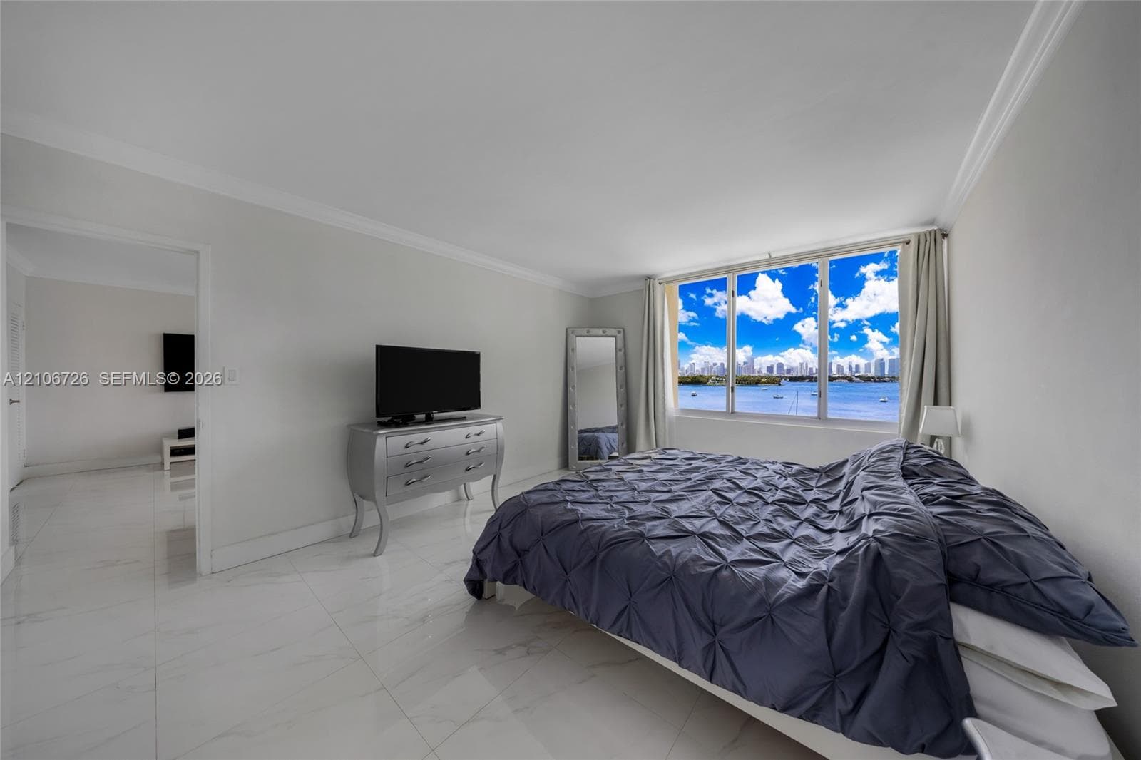 Interior space featuring polished white stone-finish flooring, crown molding, and expansive windows showcasing a water and skyline backdrop