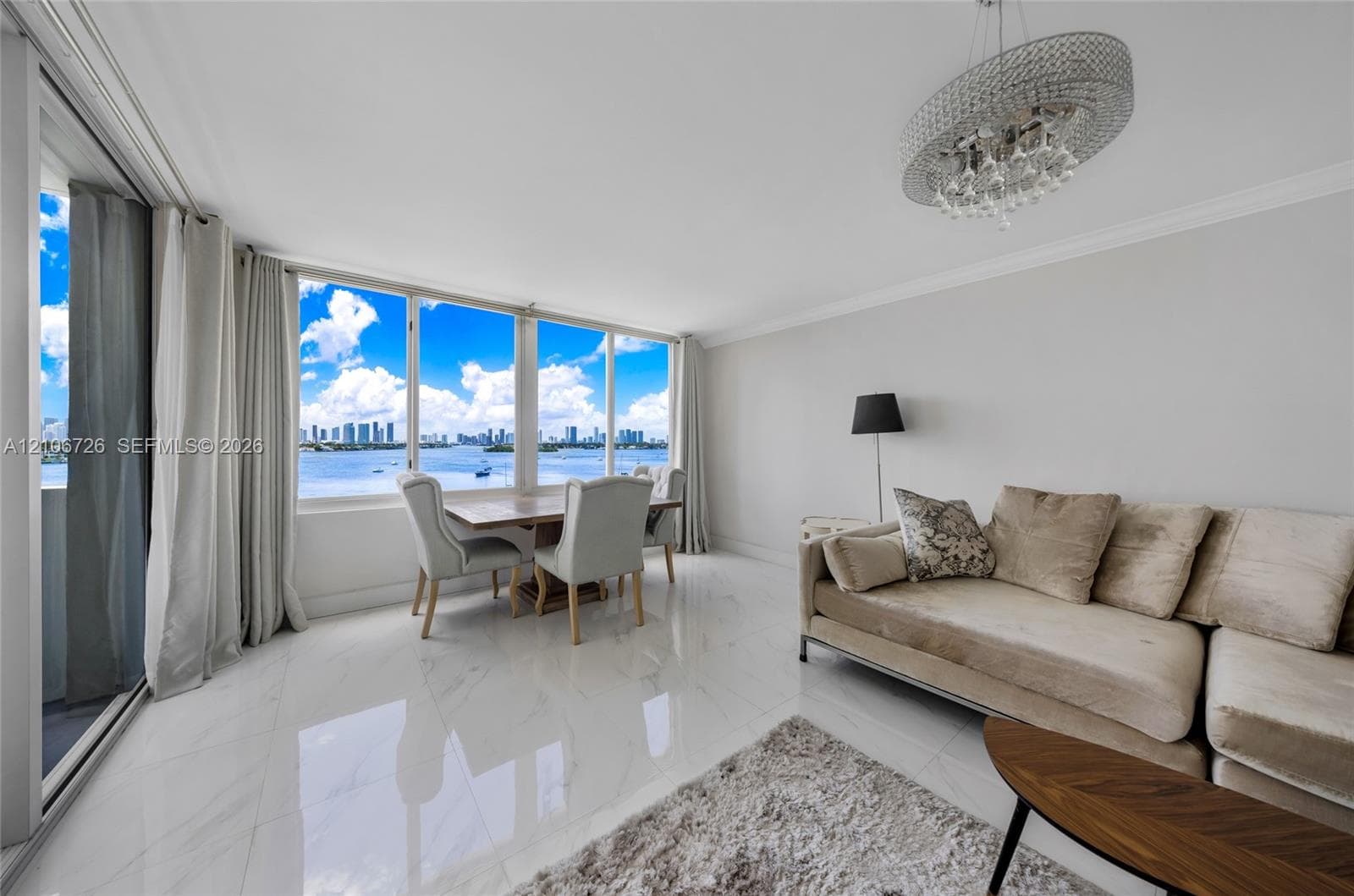 Expansive windows featuring water and city skyline scenery, floor-to-ceiling sliding glass doors, polished stone-finish tile flooring, and a crystal-accented chandelier