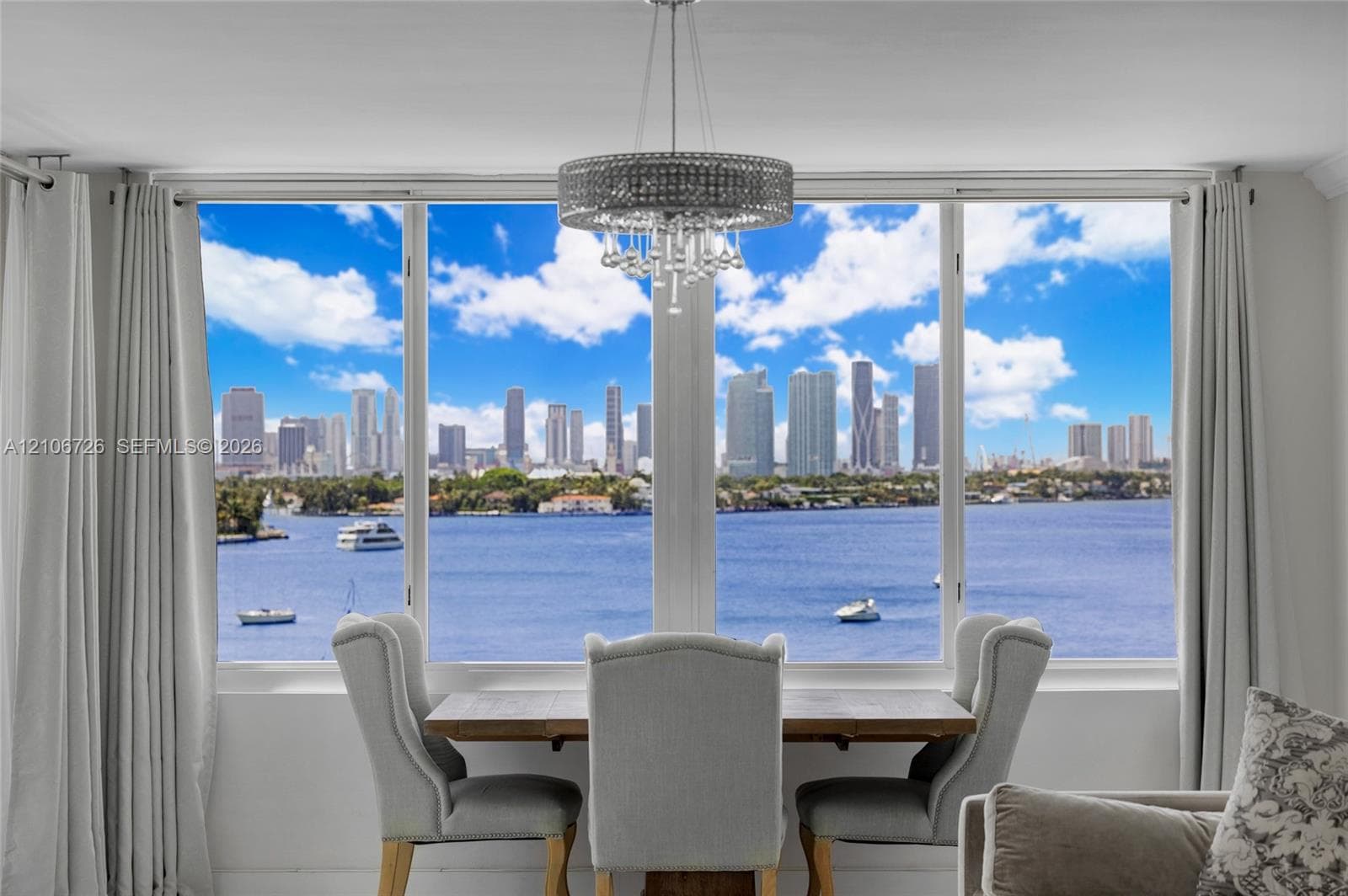 Floor-to-ceiling windows featuring panoramic water and city skyline scenery, complemented by a contemporary circular crystal drum chandelier
