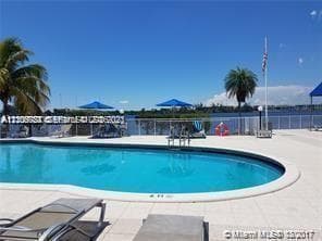 Curved swimming pool featuring a light-toned paved deck, metal safety fencing, and direct water frontage
