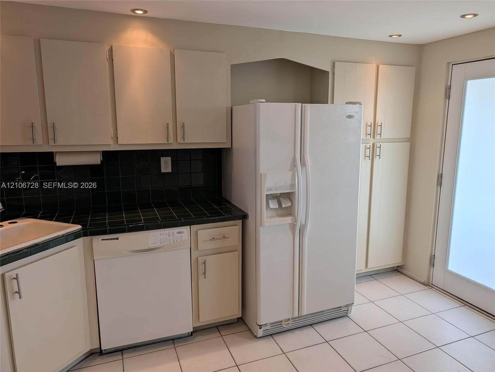 Kitchen featuring flat-panel cabinetry, tiled countertops, built-in dishwasher, side-by-side refrigerator, and tile flooring