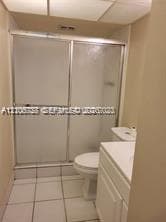 Bathroom featuring a shower stall with sliding glass doors, white tile flooring, and a white vanity cabinet