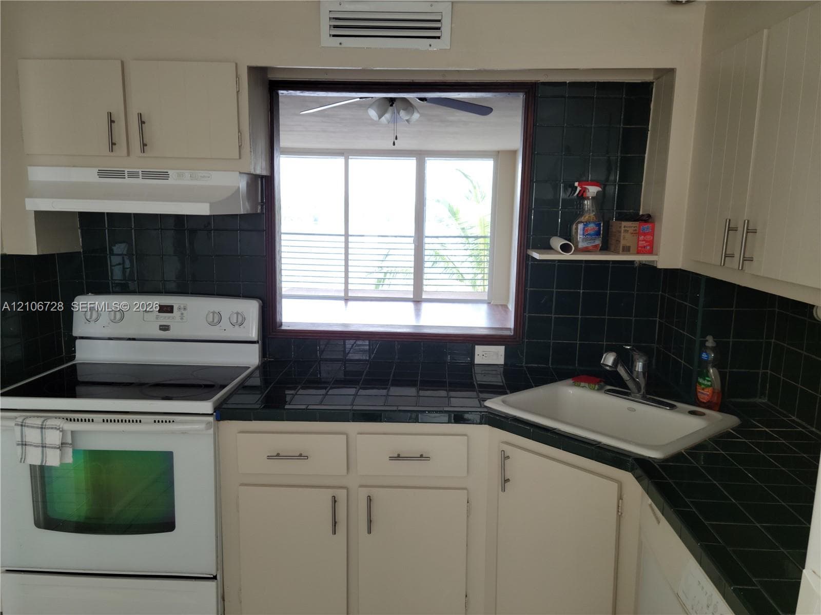 Kitchen featuring white cabinetry, dark square-tile countertops, a white top-mount sink with a chrome faucet, and a white freestanding electric range