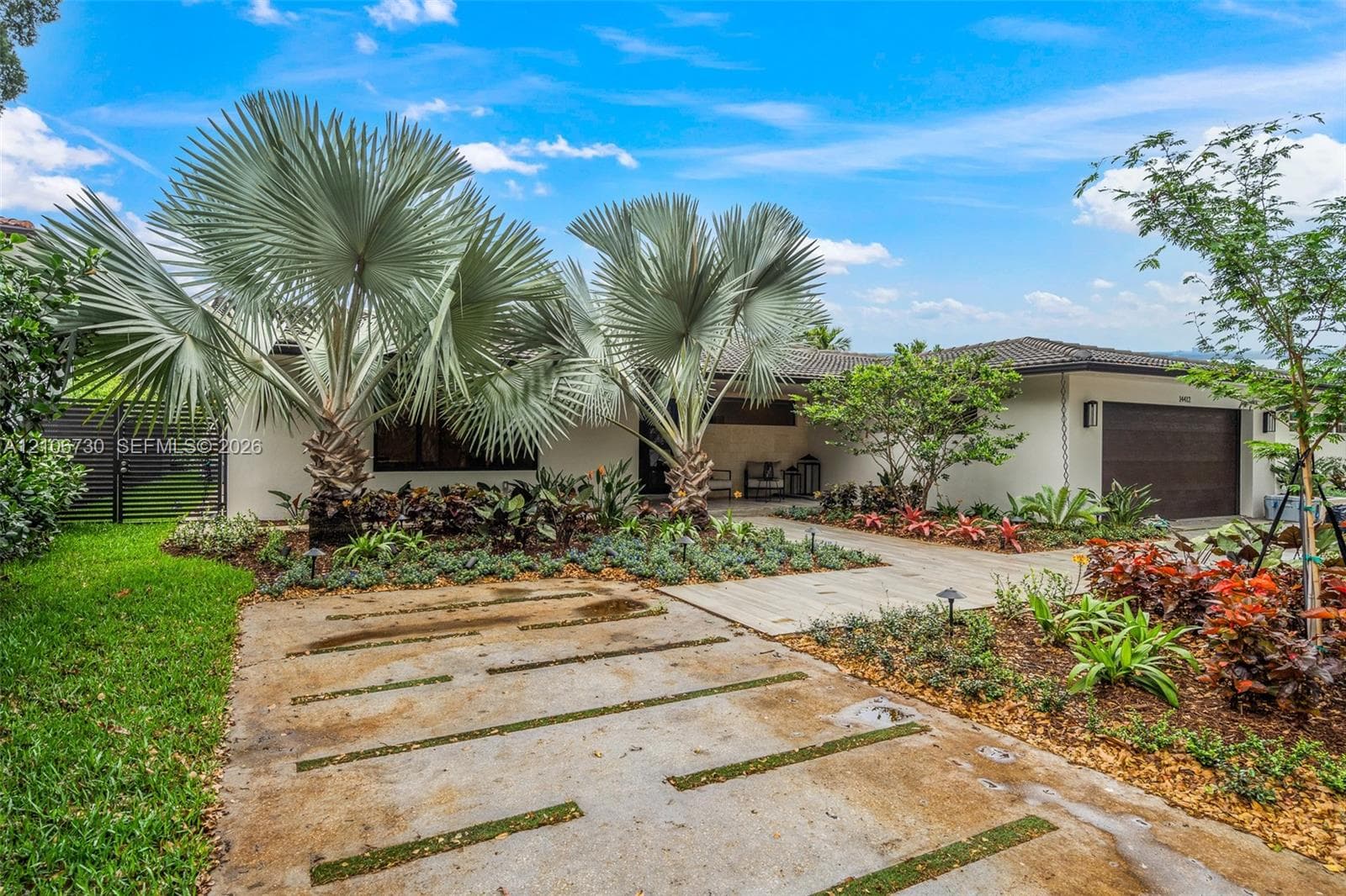 Stucco exterior featuring a multi-car garage, concrete paver driveway with integrated grass strips, and mature palm landscaping