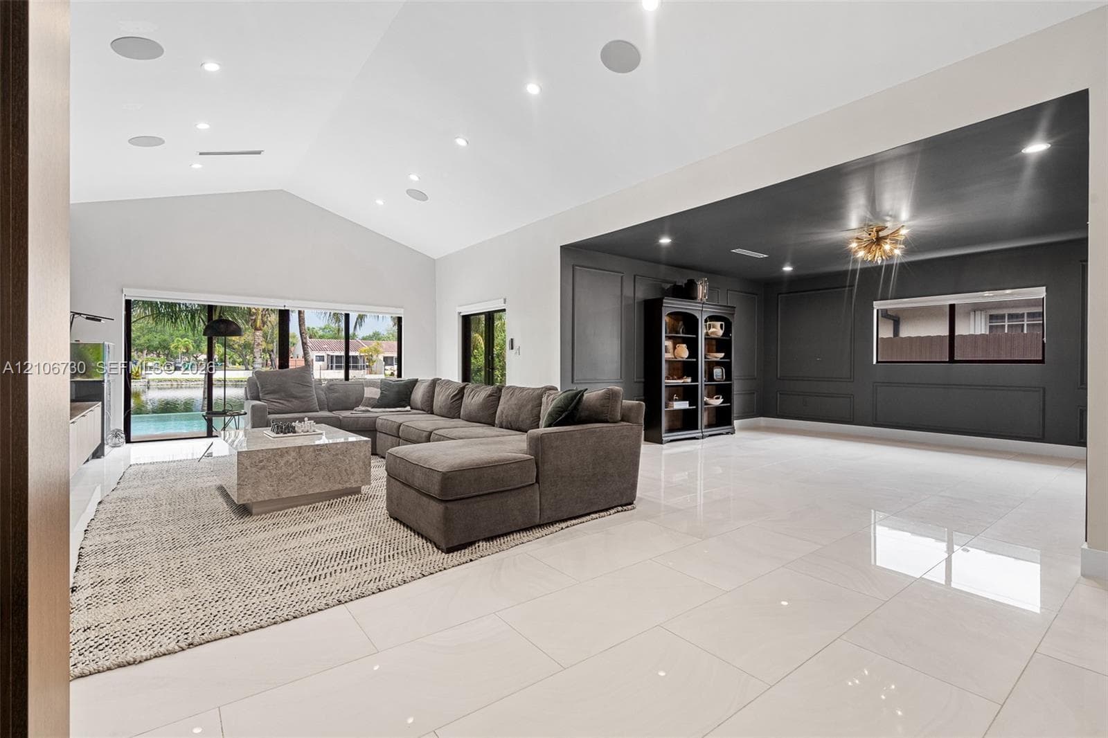 Vaulted ceilings with recessed lighting, large-format polished tile flooring, wall panel molding, and multi-panel sliding glass doors