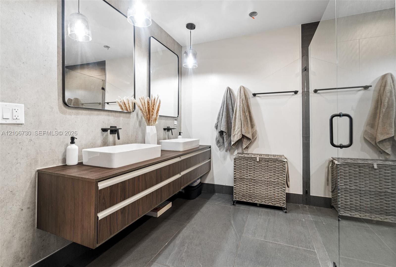 Floating wood-finish double vanity featuring white vessel sinks, matte black wall-mounted faucets, rectangular mirrors, and large-format tile flooring