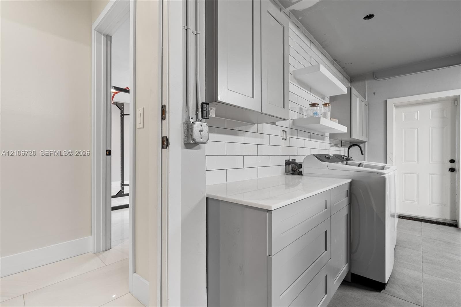 Laundry space featuring shaker-style grey cabinetry, white solid-surface countertop, white subway tile backsplash, and floating wall shelves