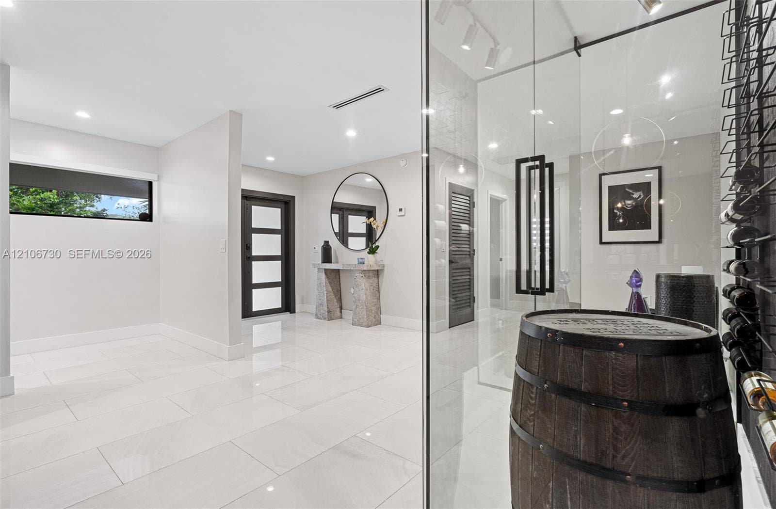 Entryway featuring large-format light tile flooring, recessed ceiling lighting, a dark-framed multi-panel front door, and a climate-controlled glass-enclosed storage area with wall-mounted racks