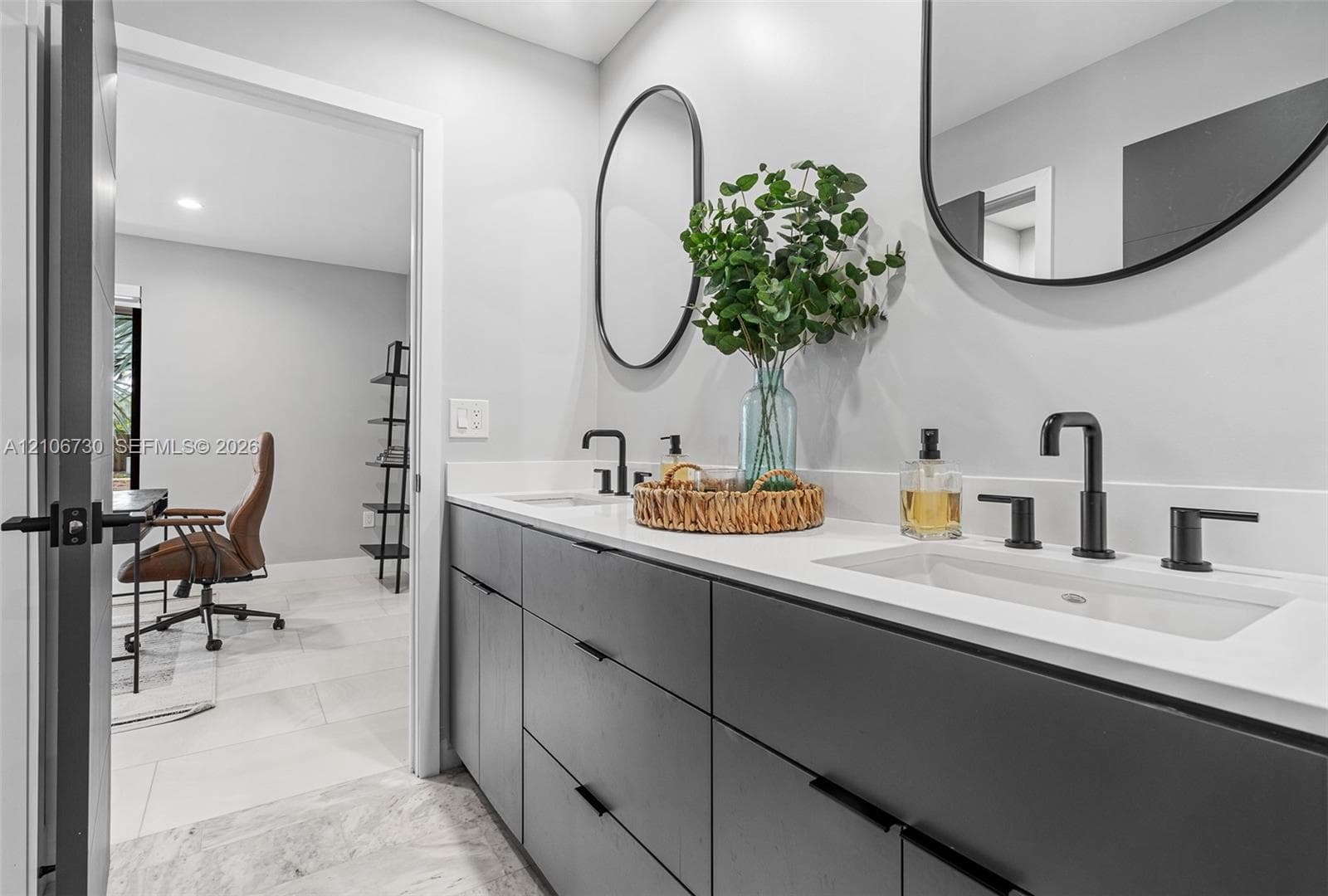 Modern dual-sink vanity featuring matte black hardware, integrated cabinetry with flat-panel doors, solid surface countertops, and dual wall-mounted oval mirrors