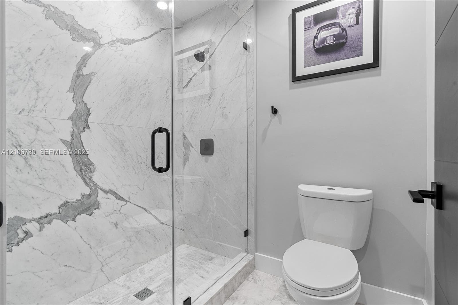 Walk-in shower featuring large-format stone-patterned tile, frameless glass enclosure, and matte black hardware, accompanied by a vitreous china toilet