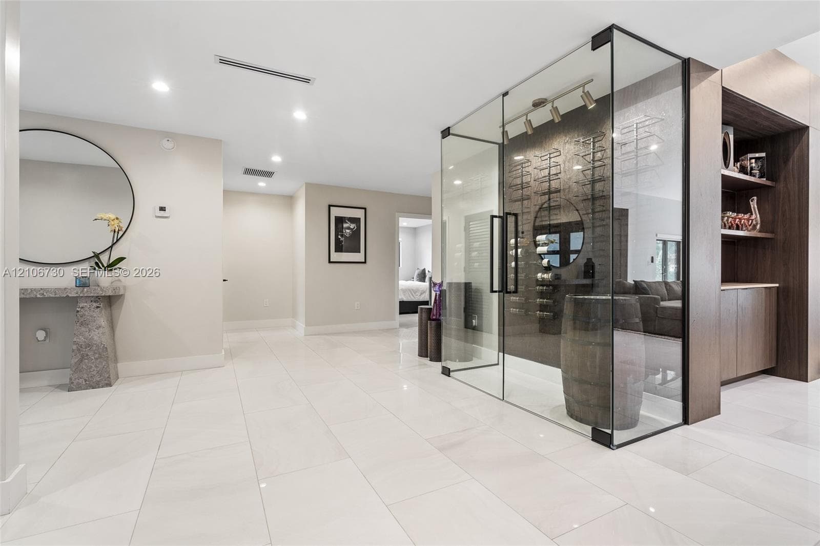 Glass-enclosed temperature-controlled wine display with wall-mounted racking, large-format tile flooring, recessed ceiling lighting, and built-in dark wood cabinetry