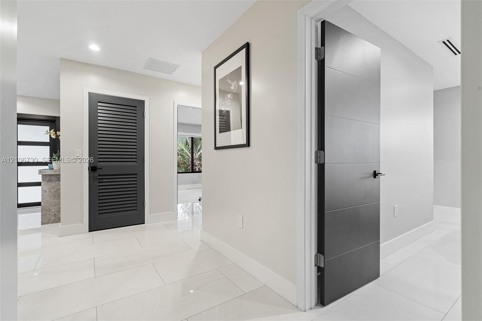 Interior hallway featuring polished large-format tile flooring, matte black lever hardware, a louvered charcoal-finished door, and a multi-panel charcoal interior door