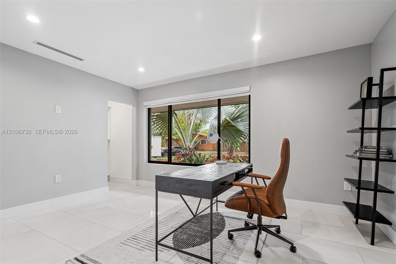 Modern home office featuring polished tile flooring, recessed ceiling lighting, and expansive multi-pane windows framing tropical landscaping