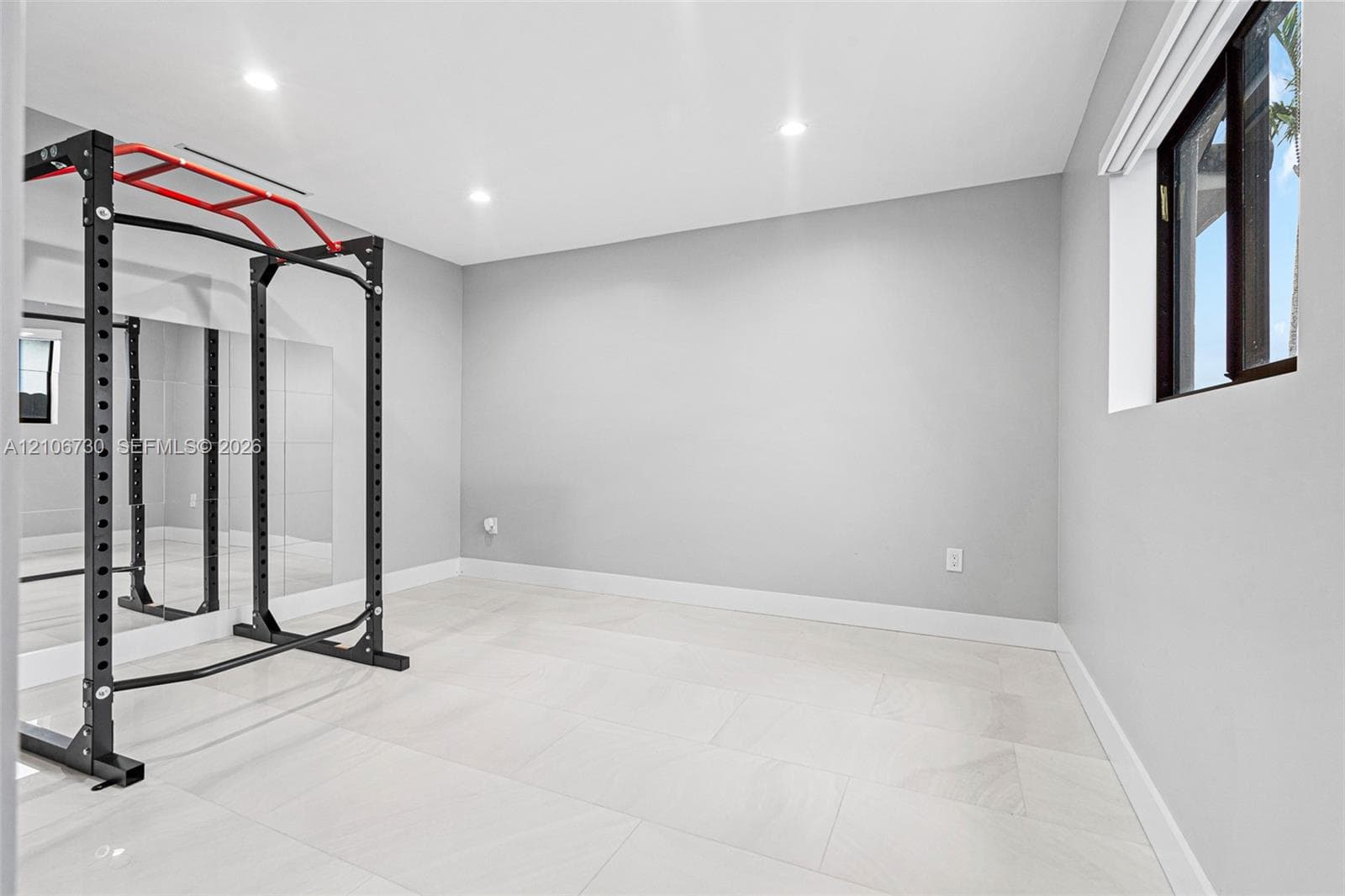Neutral interior space featuring large-format light-tone tile flooring, recessed ceiling lighting, a floor-to-ceiling wall mirror, and a single window with a dark-finish frame