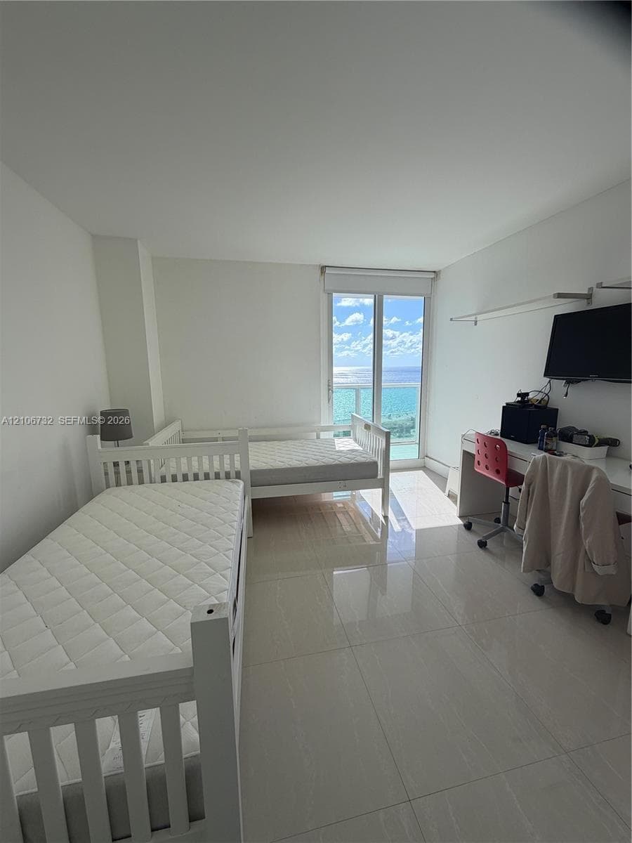Room featuring polished tile flooring, floor-to-ceiling glass door, and balcony access with ocean backdrop