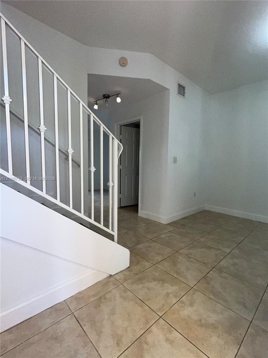 Staircase featuring white metal balusters, ceramic tile flooring, and multi-light ceiling-mounted fixture