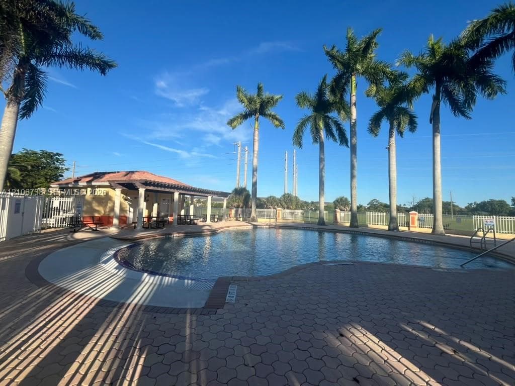 Free-form swimming pool with paver decking, covered pavilion, and mature palm trees