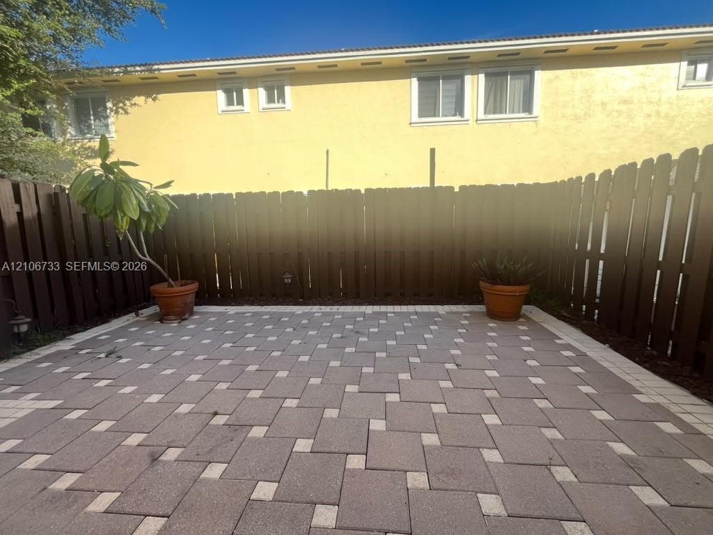 Enclosed patio featuring patterned stone pavers and a tall wooden privacy fence